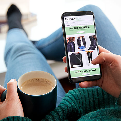 a photo of a person sitting on the couch with a cup of coffee and scrolling through the internet on their phone