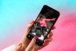 A close up image of a persons hand holding a phone and tapping on the screen with their fingers